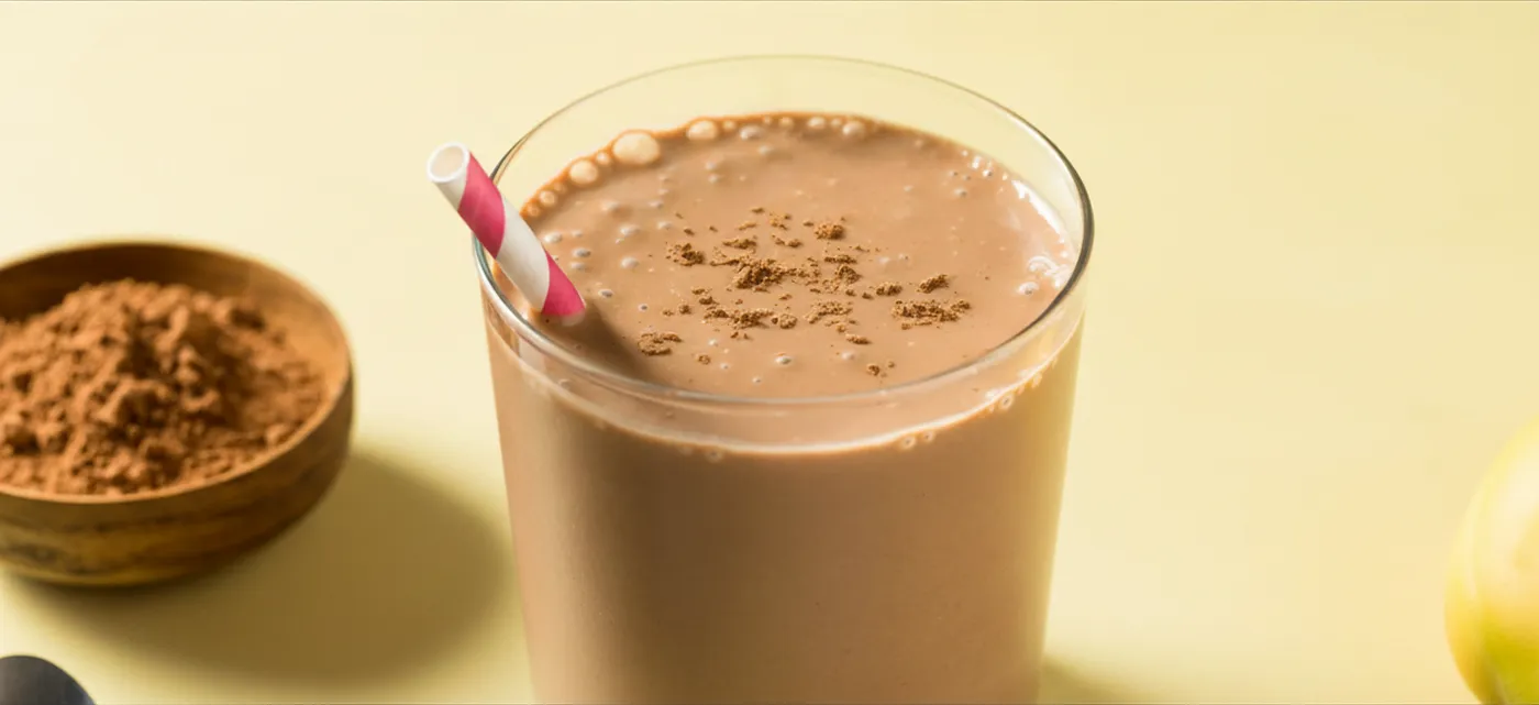 a glass of chocolate peanut butter smoothie next to cocoa powder