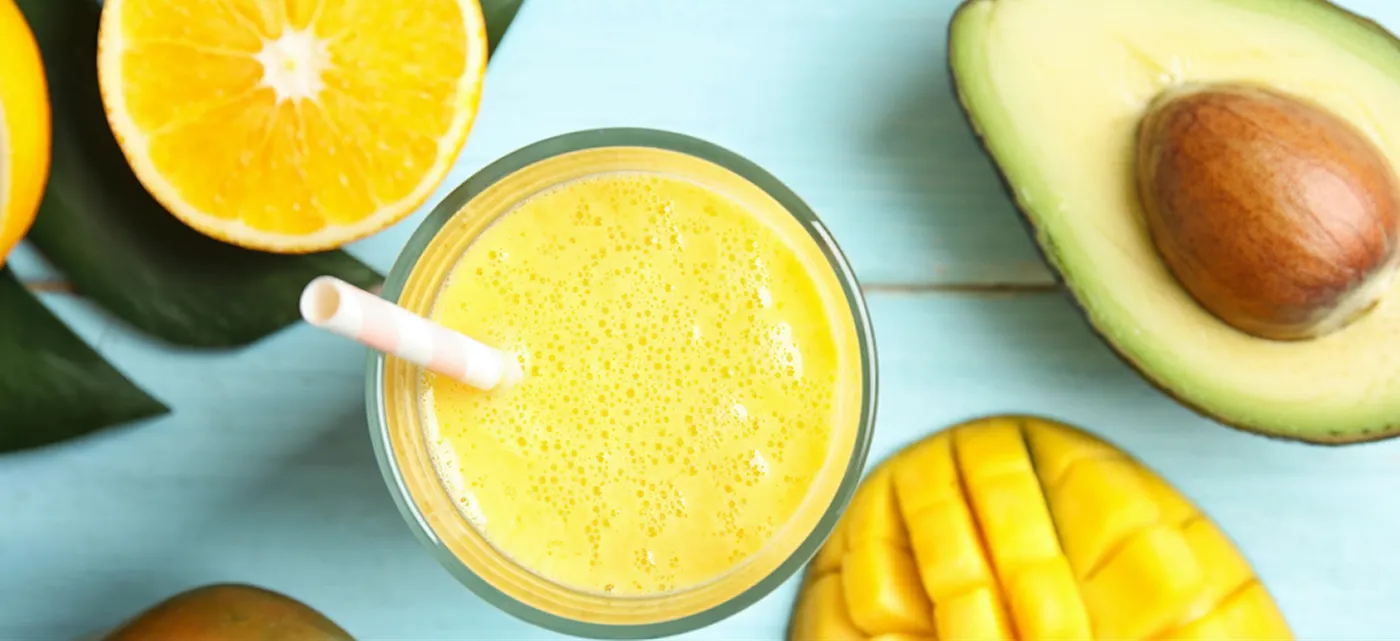 An overhead shot of a yellow tropical smoothie next to a mango and avocado